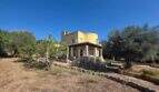 Exterior view of the yellow finca in Cala Millor with round tower, olive trees and large property under blue sky.