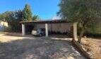 Covered carport of the finca in Cala Millor with parking spaces, concrete floor and Mediterranean vegetation.
