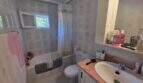 Bright bathroom of the finca in Cala Millor with bathtub, shower curtain, toilet and washbasin with wooden vanity.