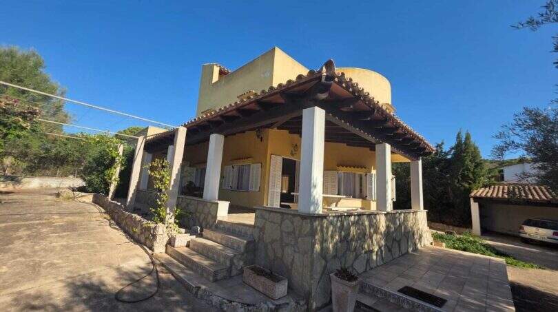 Exterior view of the finca in Cala Millor with covered terrace, white columns and yellow facade.