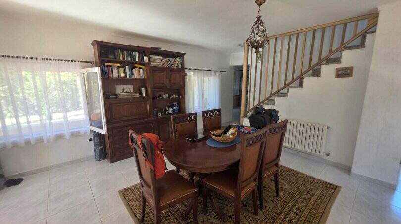 Dining room of the finca in Cala Millor with round wooden table, bookshelf and staircase to the upper floor.