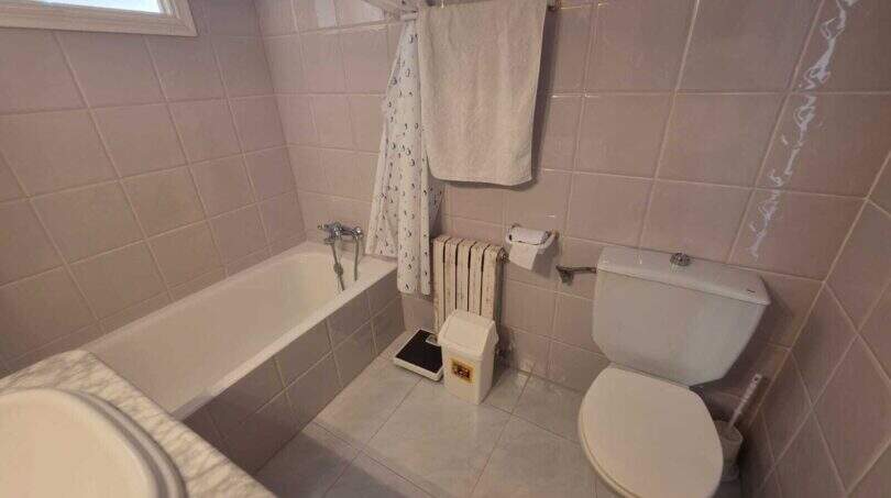 Bathroom of the finca in Cala Millor with bathtub, toilet, shower curtain and light tile floor