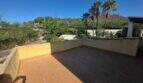 Sunny roof terrace of the finca in Cala Millor with tile flooring, palm trees and view of rocky hills.