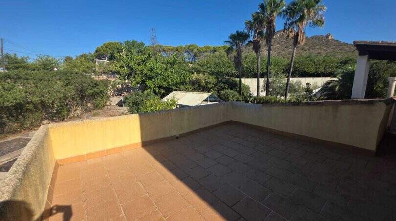 Sunny roof terrace of the finca in Cala Millor with tile flooring, palm trees and view of rocky hills.