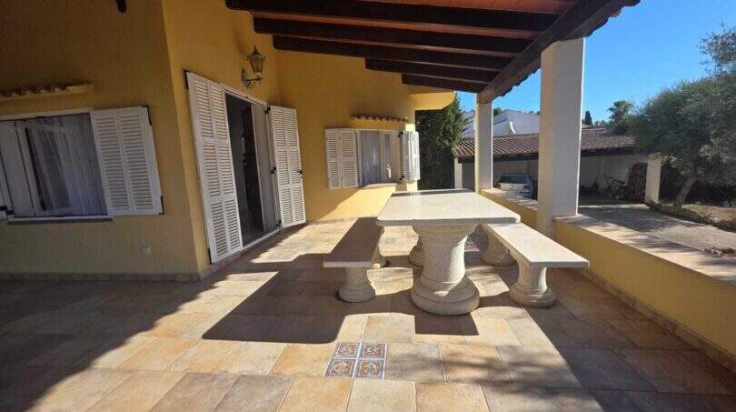 Covered terrace of the finca in Cala Millor with stone table, wooden beam ceiling and Mediterranean flair.