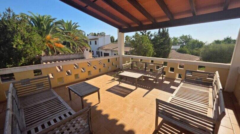 Covered roof terrace of the finca in Cala Millor with wooden furniture, stone floor and view of palm trees and neighboring villas.