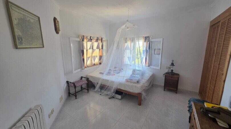 Bright bedroom of the finca in Cala Millor with mosquito net, tile floor and two windows.