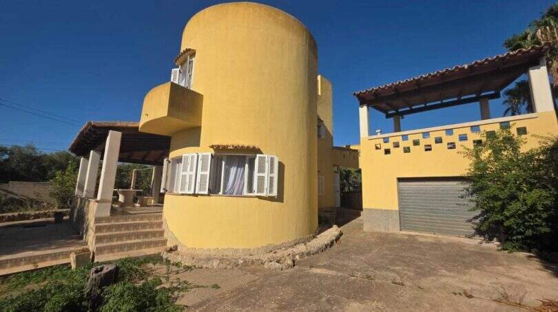 Exterior view of the finca in Cala Millor with distinctive yellow round tower facade, garage and covered terrace.