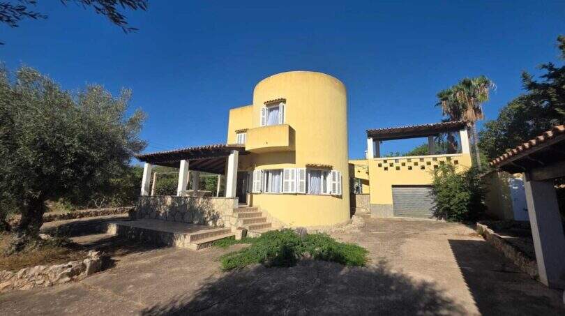 Exterior view of the yellow finca in Cala Millor with distinctive round tower, terrace and Mediterranean vegetation.