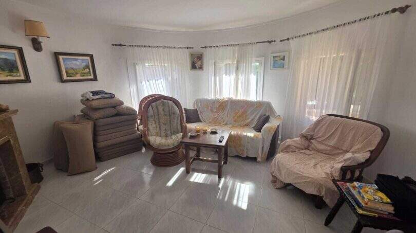 Living room of the finca in Cala Millor with fireplace, rattan armchair, sofa and large windows with curtains.