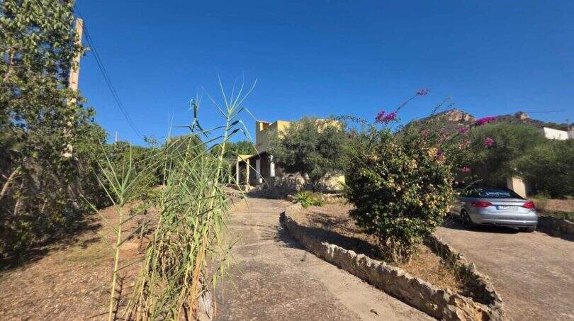 Entrance of a finca in Cala Millor with bougainvillea, natural stone walls and mountain view under blue sky.