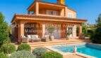 Außenansicht Villa Sa Coma mit Pool, Terrasse, Loungemöbeln und mediterranem Garten unter blauem Himmel.