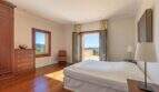 Bright bedroom of Felanitx finca with wooden floor, double bed and balcony with mountain panoramic view.