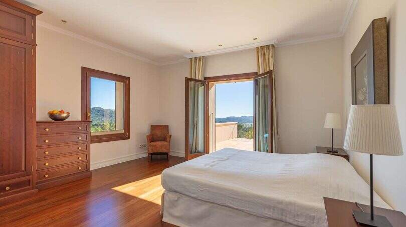 Bright bedroom of Felanitx finca with wooden floor, double bed and balcony with mountain view