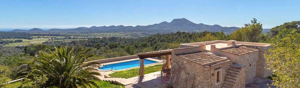 Exclusive finca in Felanitx: natural stone building with pool, pergola, palm tree and panoramic view of mountains and valley.