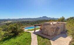 Finca exclusiva en Felanitx: edificio de piedra natural con piscina, pérgola, palmera y vistas panorámicas a las montañas y el valle.