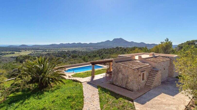 Exclusive finca in Felanitx: natural stone building with pool, pergola, palm tree and panoramic view of mountains and valley.