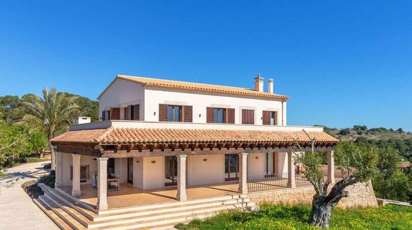Exterior view of the exclusive finca in Felanitx with Mediterranean architecture, columned veranda, terracotta roof and olive tree.