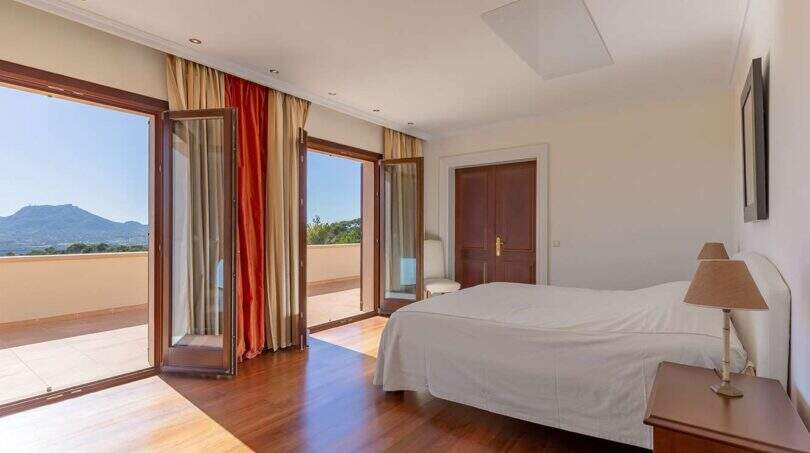 Bright bedroom of Felanitx finca with wooden floor, double bed and panoramic doors with mountain view.