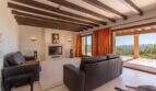 Bright living room of Felanitx finca with wooden beam ceiling, leather sofas, fireplace and panoramic view of the mountains.