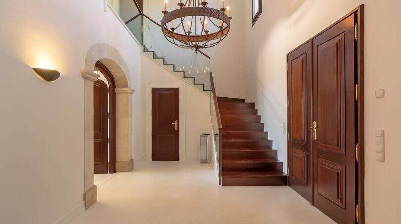 Elegant entrance area of the finca in Felanitx with wooden staircase, chandelier and dark wooden doors
