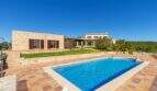 Exclusive finca in Felanitx with large swimming pool, natural stone walls, palms and well-maintained garden under blue sky.