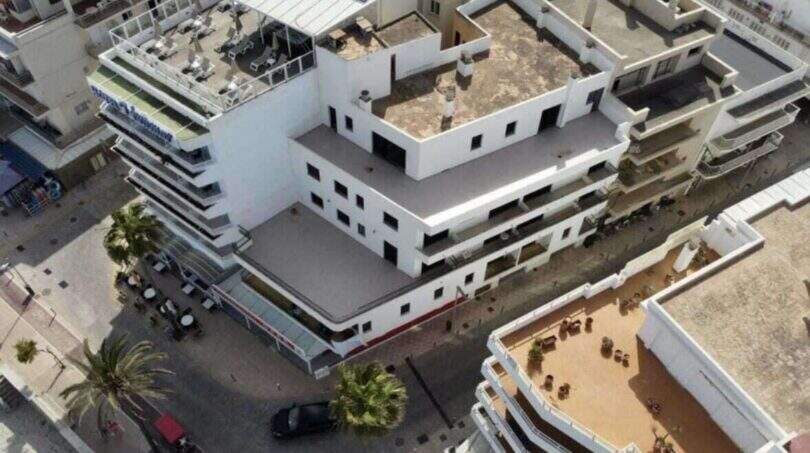 Luftaufnahme eines weißen Hotelgebäudes in Cala Millor mit Dachterrasse, Balkonen und Palmen in erster Meereslinie.