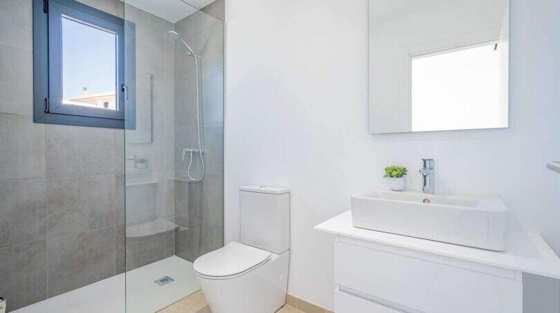 Baño luminoso de la villa nueva en Cala Romántica con ducha de cristal, lavabo moderno e inodoro.