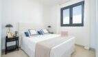 Dormitorio luminoso de la villa nueva en Cala Romántica con cama doble, mesitas de noche oscuras y ventana gris.
