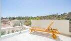 Azotea soleada de la villa nueva en Cala Romántica con tumbona de madera, barandilla de cristal y vistas a las colinas.