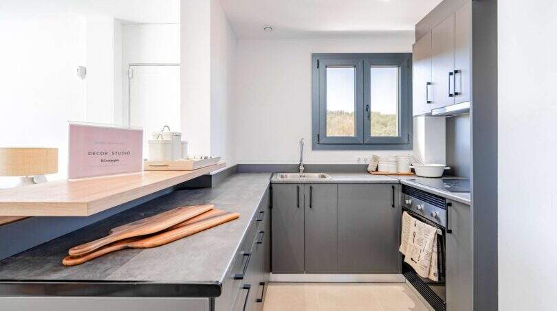 Cocina moderna de la villa nueva en Cala Romántica con armarios empotrados grises, isla de cocina y ventana con vistas a la naturaleza.