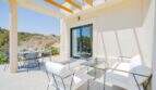 Terraza cubierta de la villa nueva en Cala Romántica con muebles lounge blancos y vistas al verdor.