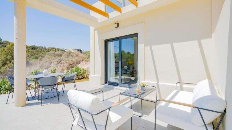 Terraza cubierta de la villa nueva en Cala Romántica con muebles lounge blancos y vistas al verdor.