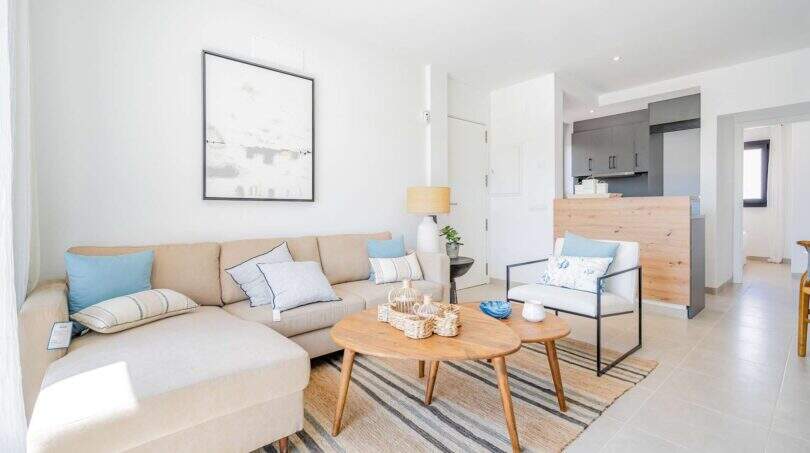 Salón luminoso de la villa nueva en Cala Romántica con sofá de arena, mesa de madera y zona de cocina abierta.