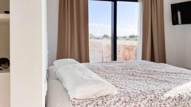Helles Schlafzimmer der Luxusfinca in Ses Salines mit Doppelbett, Blumendecke und Fenster mit Meerblick.