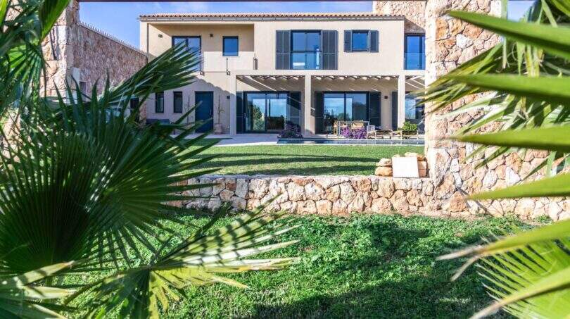 Luxusfinca Ses Salines: Gartenansicht mit Pool, Natursteinmauer und moderner Terrasse umgeben von Palmen.