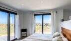 Helles Schlafzimmer der Luxusfinca Ses Salines mit Doppelbett, Holzkopfteil und Panoramafenstern mit Gartenblick.