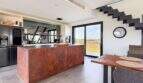Moderne Küche mit Kochinsel aus Cortenstahl, Panoramafenster und Treppe in mediterraner Luxusfinca Ses Salines