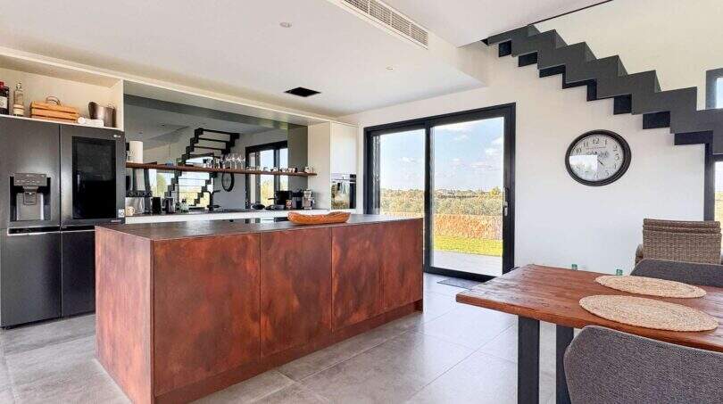 Moderne Küche mit Kochinsel aus Cortenstahl, Panoramafenster und Treppe in mediterraner Luxusfinca Ses Salines