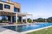 Luxusfinca Ses Salines: Infinity-Pool mit Pergola, Sonnenliegen und mediterranem Garten bei strahlendem Himmel.