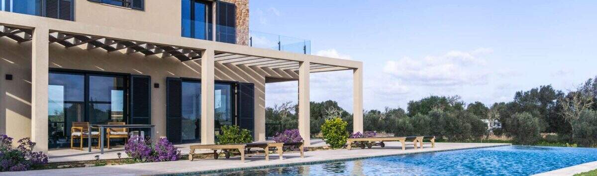 Luxusfinca Ses Salines: Infinity-Pool mit Pergola, Sonnenliegen und mediterranem Garten bei strahlendem Himmel.