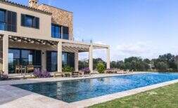 Luxusfinca Ses Salines: Infinity-Pool mit Pergola, Sonnenliegen und mediterranem Garten bei strahlendem Himmel.