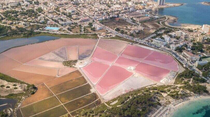 Luftbild: Rosa Salinen von Ses Salines, Küstenstadt und türkisblaues Meer bei mediterraner Luxusfinca.