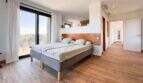 Helles Schlafzimmer der Luxusfinca in Ses Salines mit Doppelbett, Holzboden und großer Glasfront mit Balkonzugang.