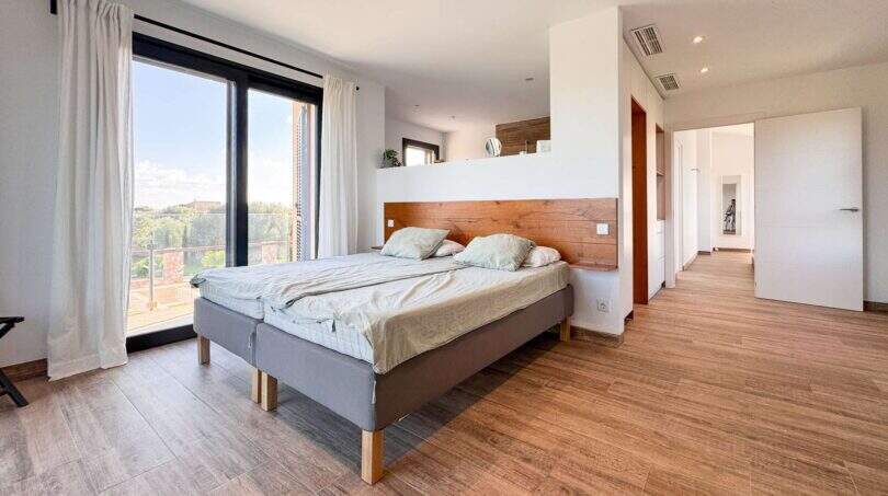 Helles Schlafzimmer der Luxusfinca in Ses Salines mit Doppelbett, Holzboden und großer Glasfront mit Balkonzugang.