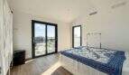 Helles Schlafzimmer der Luxusfinca in Ses Salines mit Holzboden, blauer Tagesdecke und Terrassenzugang
