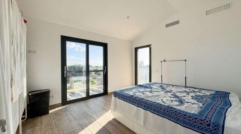Helles Schlafzimmer der Luxusfinca in Ses Salines mit Holzboden, blauer Tagesdecke und Terrassenzugang