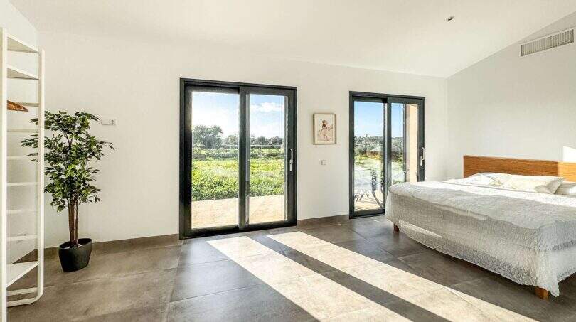 Helles Schlafzimmer der Luxusfinca in Ses Salines mit Terrassenzugang und Blick auf grüne Landschaft