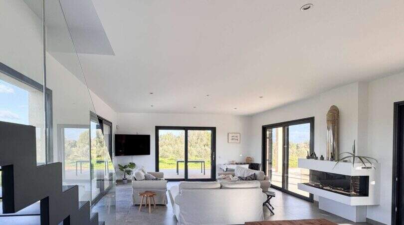 Helles Wohnzimmer der Luxusfinca mit Kamin, weißen Sofas und Panoramafenstern mit Naturblick.