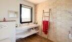 Modernes Badezimmer der Luxusfinca mit schwebendem Waschtisch, Bambus-Leiter und beiger Fliesenwand mit Dusche.